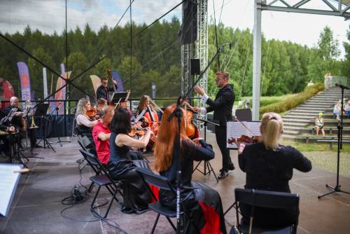 Muzycy podczas koncertu na scenie. Stroje czarno-czerwone. Widok zza pleców smyczków.