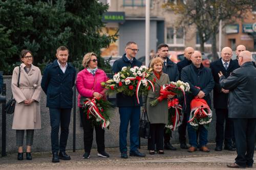 Przedstawiciele władz lokalnych stojący przed tłumem z kwiatami.