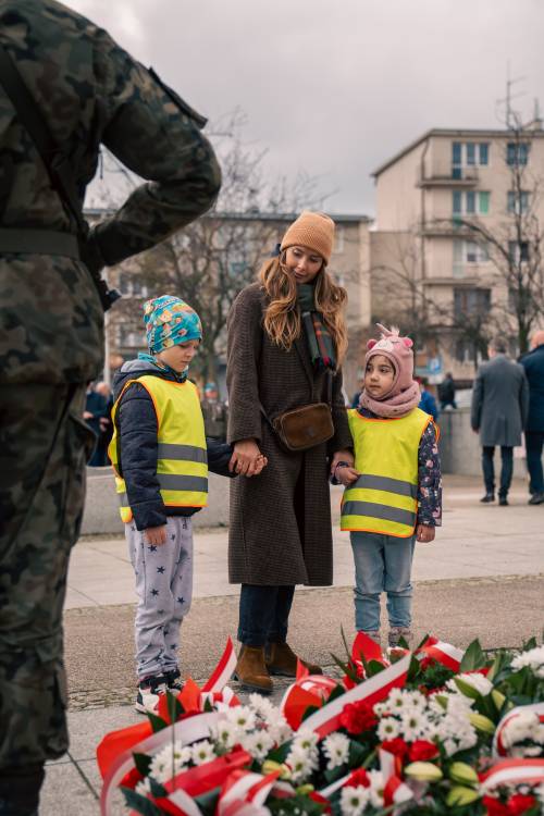 Przedszkolaki z opiekunką składają kwiaty pod pomnikiem Nike.