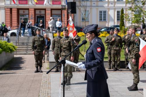 Przy mównicy przedstawicielka policji. W tle budynek Starostwa Powiatowego i żołnierze.