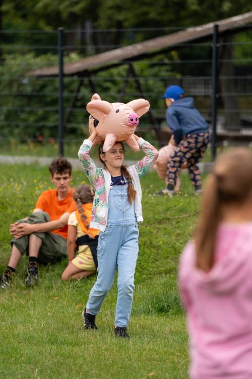 Dziewczynka niesie dmuchaną świnkę nad głową.