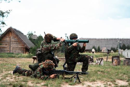 Zdjęcie przedstawia aktywności podczas Drop Zone w Faktorii Handlowej.  Trzech rekonstruktorów demonstruje strzelanie z broni palnej.