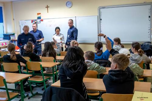 Rozpoczęcie Turnieju o bezpieczeństwie w Ruchu Drogowym - część teoretyczna. Organizatorzy stojący pod tablicą, uczestnicy siedzący w ławkach. Uczestnicy zgłaszają się do odpowiedzi.