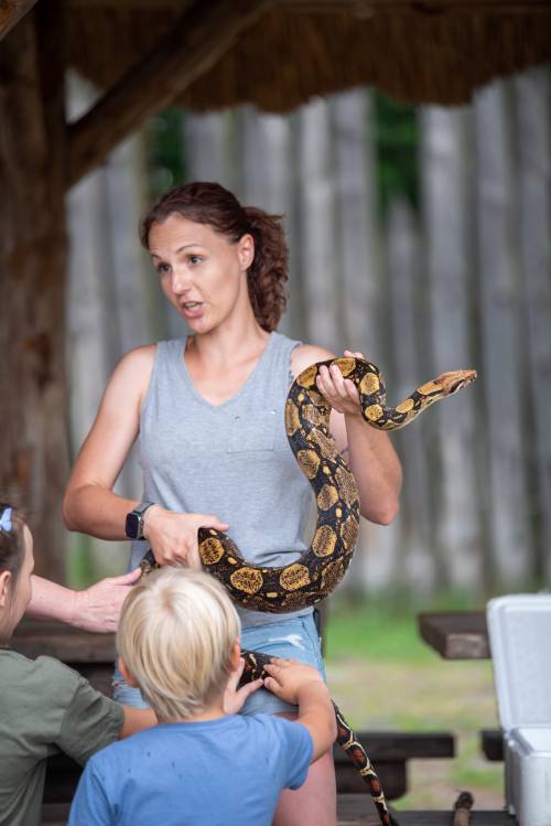 Kobieta trzyma w ręce węża, przyglądają się jej dzieci