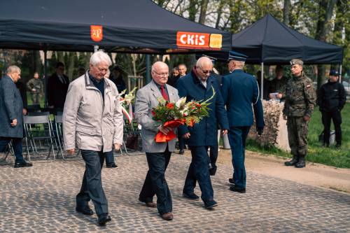 Goście składają kwiaty podczas obchodów upamiętniających zbrodnię katyńską w obstawie żołnierzy.