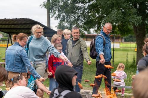 Uczestnicy pieką kiełbaski nad ogniskiem.