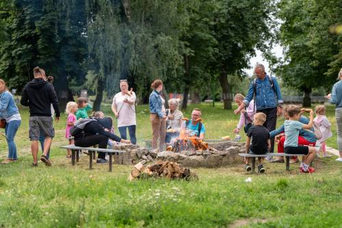 Uczestnicy pieką kiełbaski nad ogniskiem. Szeroki kadr.