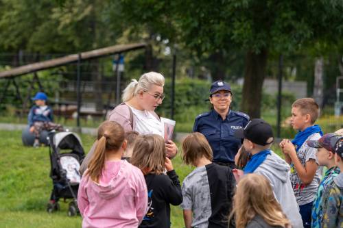 Policjantka i cywil instruują dzieci. W tle wózek dziecięcy.