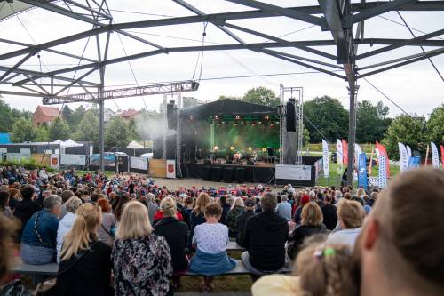 Czterech muzyków na scenie. Szeroki kadr zza pleców publiczności.