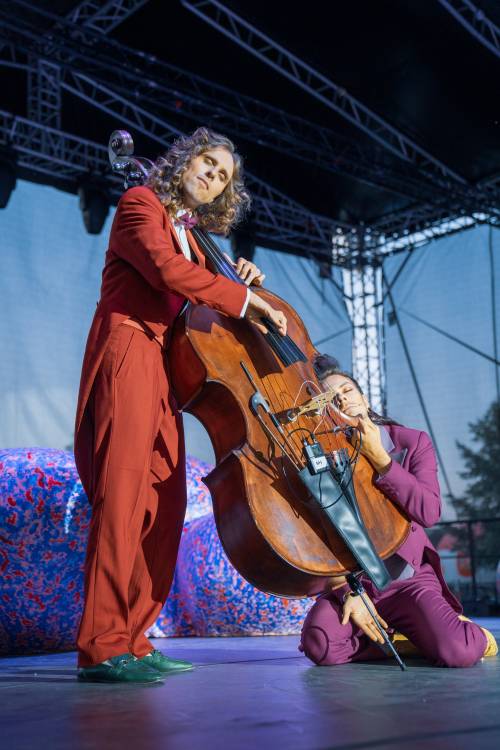 Na scenie stoi kontrabasista oraz obok klęczy mężczyzna przytulony do instrumentu na scenie.