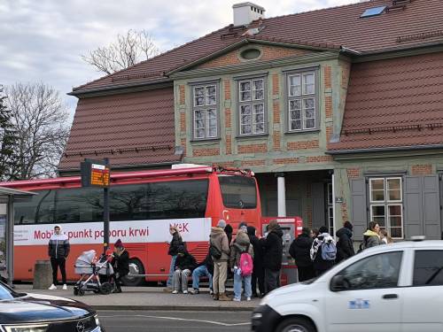 Widok ruchliwej ulicy, osoby kłębiące się przy krwiobusie, chcące oddać krew.