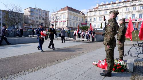Goście składają kwiaty pod pomnikiem Nike. Z kwiatami przedstawiciele służb mundurowych.