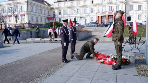 Goście składają kwiaty pod pomnikiem Nike. Z kwiatami przedstawiciele służb mundurowych.