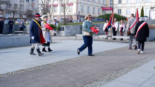 Goście składają kwiaty pod pomnikiem Nike. Z kwiatami przedstawicielka organizacji pozarządowej i związku Kaszubów w strojach ludowych..