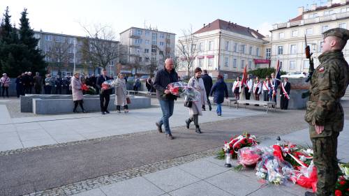 Goście składają kwiaty pod pomnikiem Nike. Z kwiatami przedstawiciele szkół.