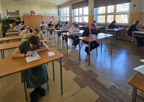 Uczestnicy siedzą w ławkach pisząc test wiedzy.