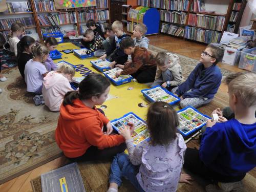 Grupa dzieci siedząca na macie z zestawami kloców i tabletami.