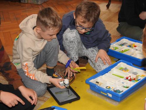 Grupa dzieci siedząca na macie z zestawami kloców i tabletami. Zbliżenie na dwóch chłopców.