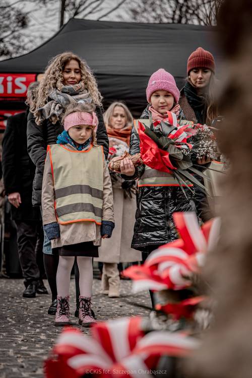 Dzieci i opiekunowie składają kwiaty podczas uroczystości.
