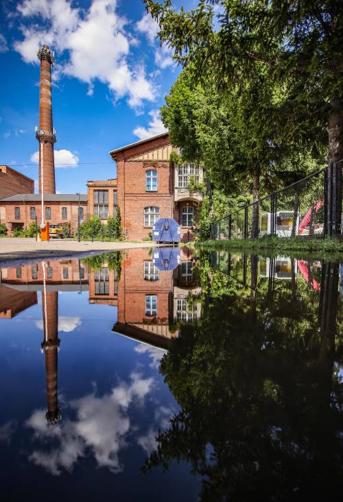 Plac cukrowni - widok odbity w tafli wody w kałuży.