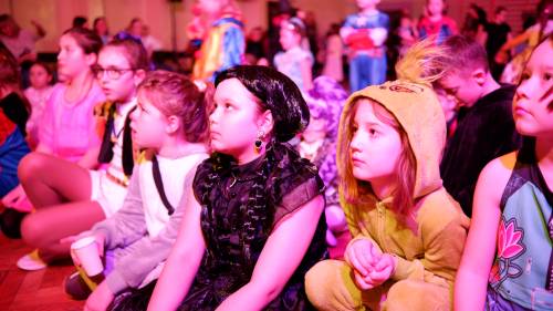 Dzieci w strojach karnawałowych siedzą przed sceną