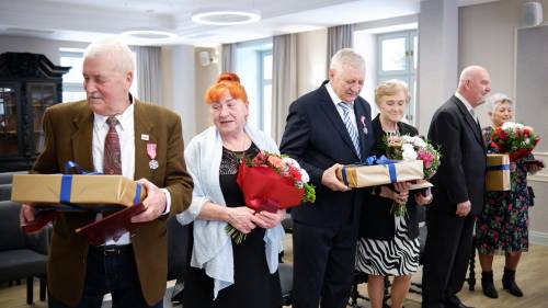 Trzy pary jubilatów z kwiatami i prezentami