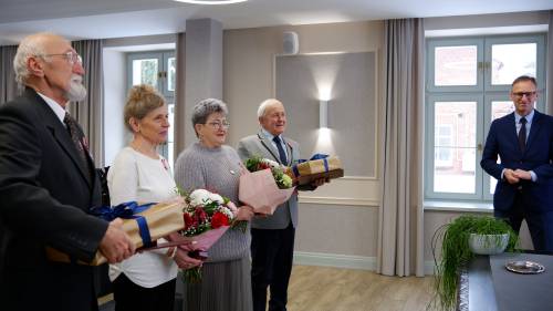 Dwie pary jubilatów z kwiatami i prezentami