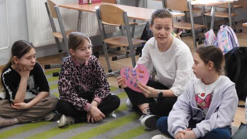 Pani siedzi z dziećmi na podłodze i pokazuje dzieciom serce z papieru