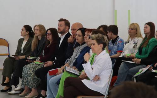 Uczestnicy sejmiku siedzą na krzesłach i słuchają debaty