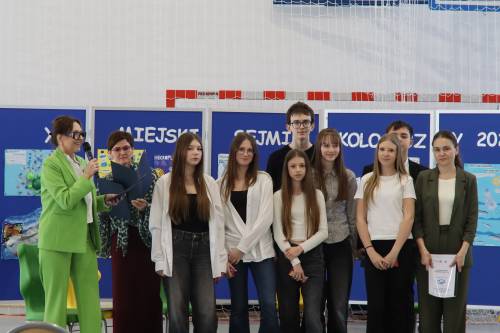 Grupa nagrodzonych uczniów i uczennic stoi obok nauczycielki i dyrektor szkoły