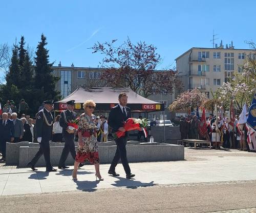 Uczestnicy uroczystości idą z wiązankami kwiatów