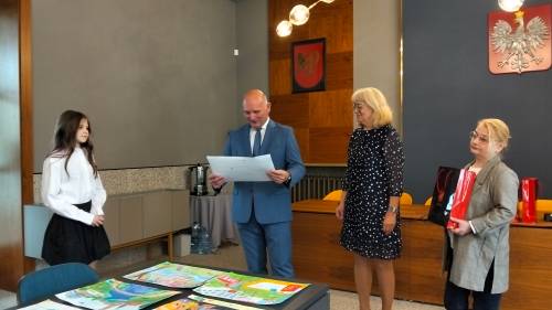 Zastępca burmistrza ogląda jedną z prac nagrodzonych, obok stoi laureatka i kierownik biblioteki
