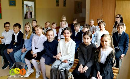 Uczestnicy konkursu siedzą na ławeczkach na szkolnym holu