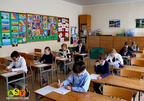 Dzieci siedzą w ławkach i rozwiązują zadania