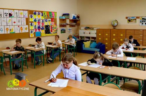 Dzieci siedzą w ławkach i rozwiązują zadania