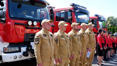 Strażacy i drużyny młodzieżowe stoją przed strażackimi pojazdami