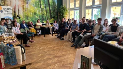 Uczniowie, zaproszeni goście i pedagodzy siedzą na krzesłach w bibliotece