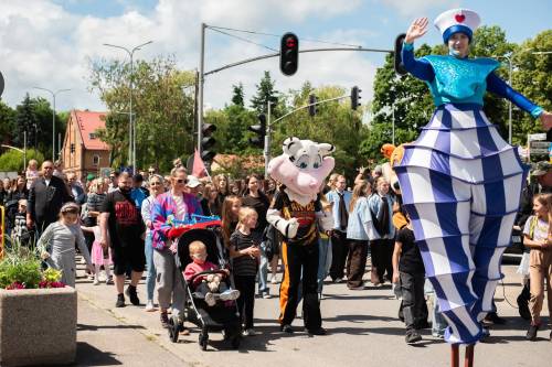 Uczestnicy parady idą ulicą, na przedzie szczudlarz