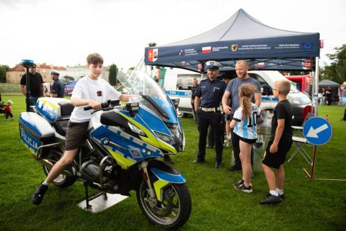 Chłopiec siedzi na policyjnym motocyklu, obok stoi dwójka dzieci, mężczyzna i policjant