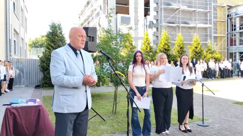 Dyrektor szkoły przemawia do mikrofonu, z tyłu stoją uczniowie
