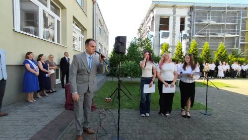 Zastępca burmistrza przemawia do mikrofonu, z tyłu uczniowie i nauczyciele