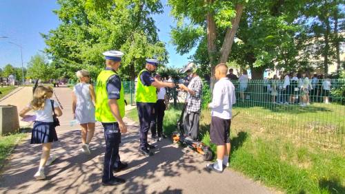 Policjant legitymuje młodego chłopaka z hulajnogą, obok inny chłopiec i policjant