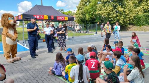 Grupa dzieci siedzi na ziemi i patrzy na policjanta