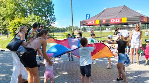 Dzieci i rodzice trzymają w rękach dużą, kolorową chustę