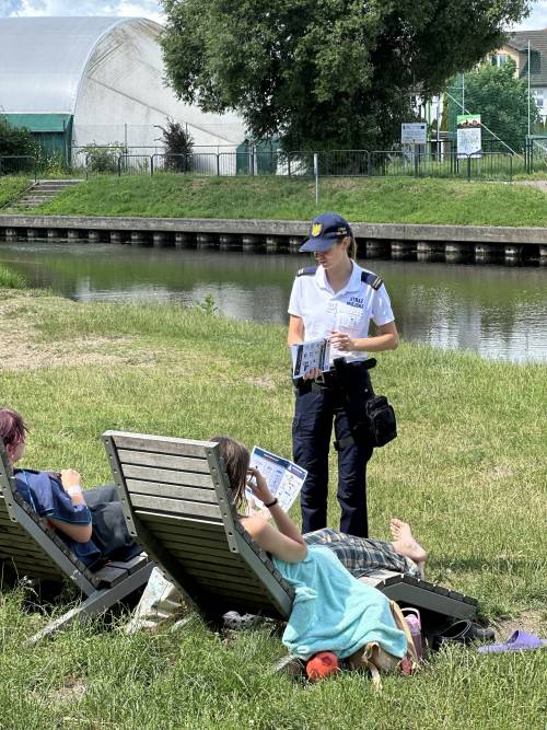 Strażniczka miejska pokazuje ulotki dwóm kobietom leżącym na leżakach