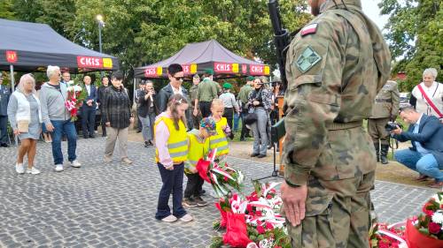 Trójka przedszkolaków z panią składają kwiaty