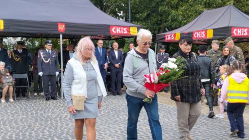 Dwie pani i pan z kwiatami, w tle inni uczestnicy uroczystości