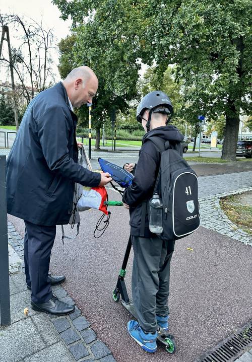 Mężczyzna wręcza chłopcu na hulajnodze torbę