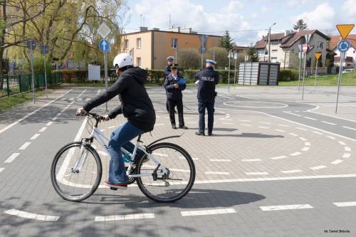 Rowerzysta poruszający się po miasteczku rowerowym przy SP3. Mundurowi oceniający przejazd konkursowy w tle.