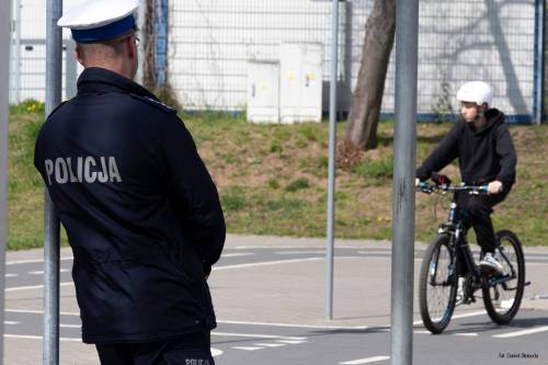 Mundurowy tyłem oceniający zawodnika. Uczestnik na rowerze przejeżdża przez tor.